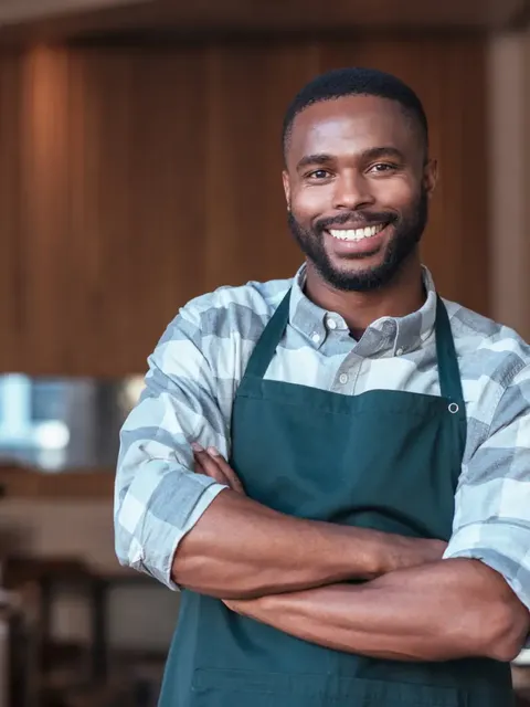 Smiling cafe owner with arms crossed in his coffee shop