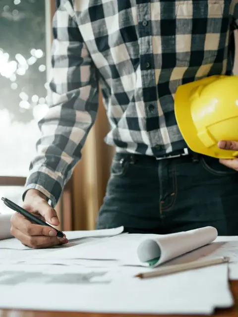 Contractor marking up building plans while holding a hard hat